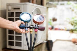 A hand holding a two-dial device with hoses attached to a mini-split system.