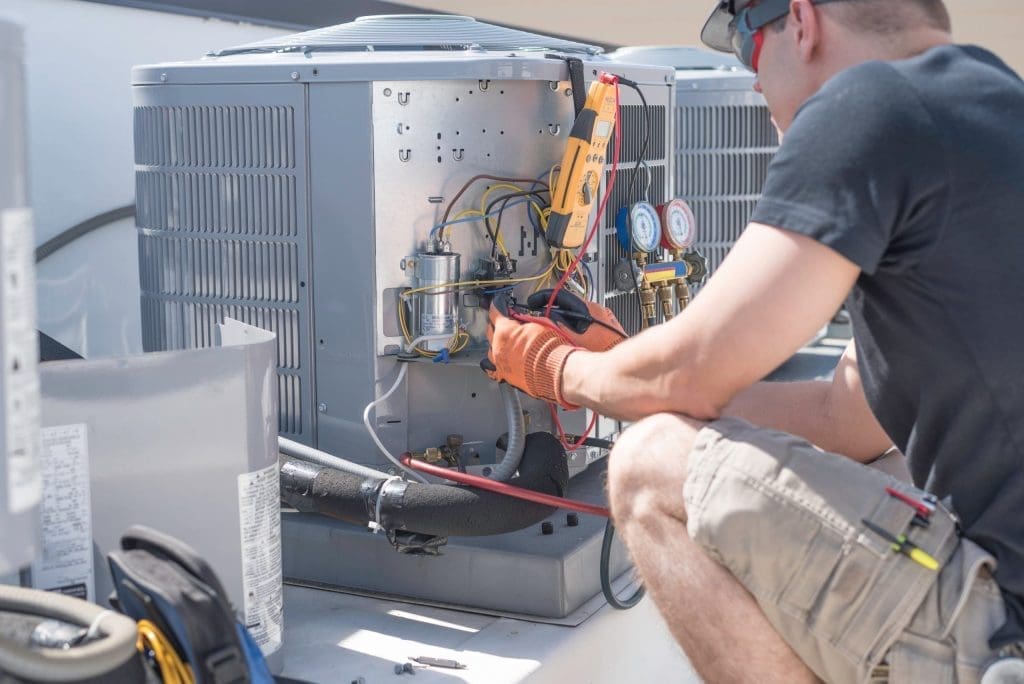 An HVAC technician checking the wiring of an outdoor unit