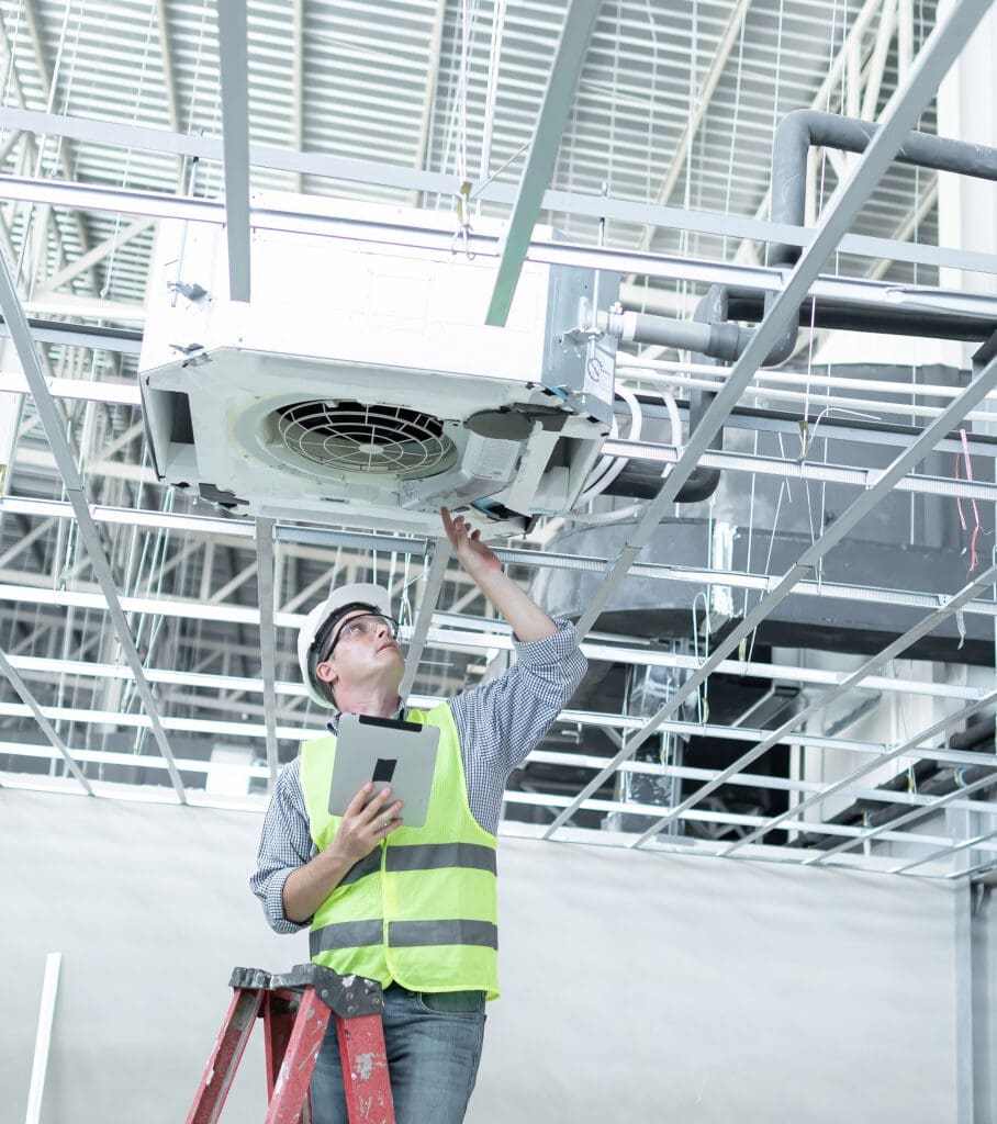 A commercial HVAC contractor inspecting a fan unit in an industrial building
